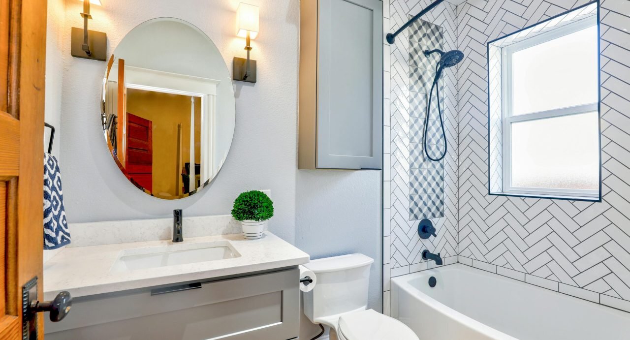 Elegant modern bathroom featuring chevron tiles, oval mirror, and sleek fixtures for a contemporary look.