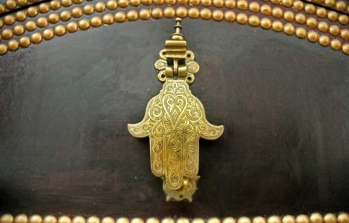 Beautiful brass Hamsa door knocker with intricate detailing on a wooden surface, offering cultural and artistic appeal.